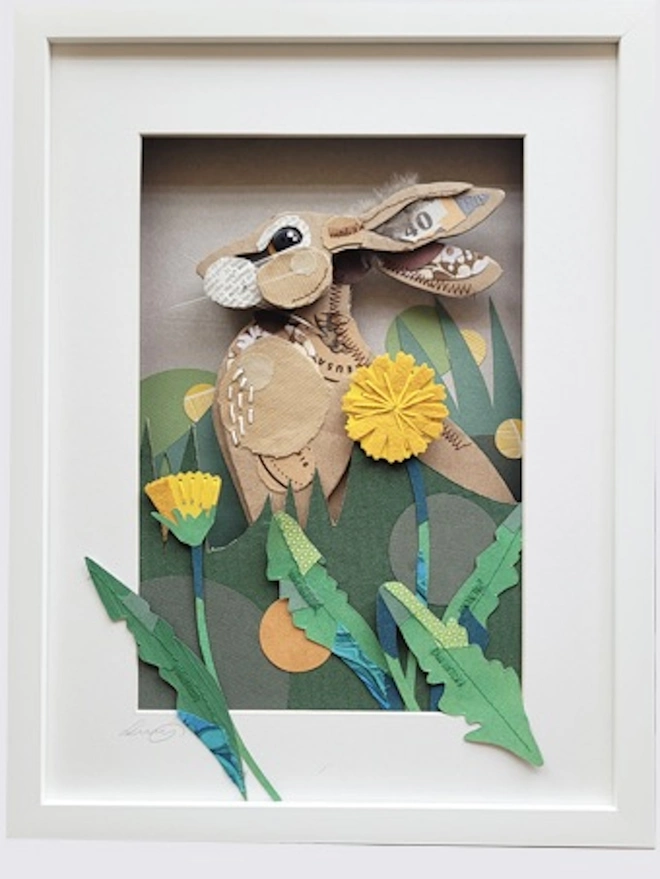 Alert upright hare nestled in long grass with dandelions in the foreground. Made with layers of corrugated card to create a 3-D effect. Decorated with stitched vintage fabric and torn brown papers.