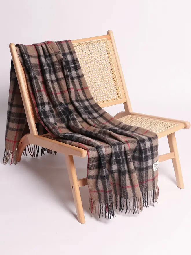 Camel Thompson Recycled Wool Blanket, a brown blanket draped over a wooden chair on a white surface against a plain backdrop. 