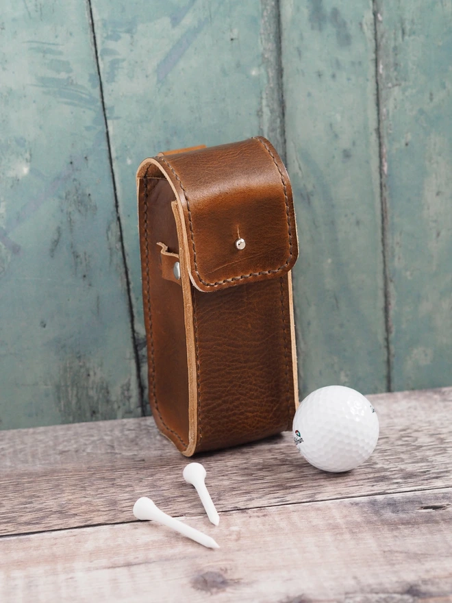 Handmade leather golf ball pouch. A hand holds a golf ball waiting to put it inside the pouch which can carry up to 3 balls.