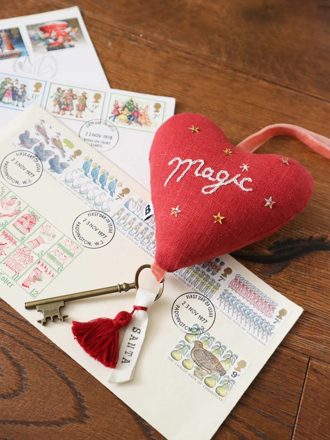 Linen heart ornament with Magic embroidery, hanging rustic key with Santa's name tag and red tassles, surrounded by Christmas letters.