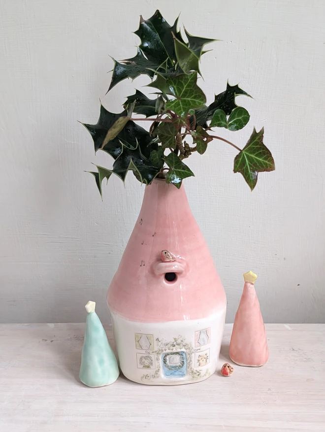 bud vase with a pink roof and robin with windows and lady and cat looking out of them 