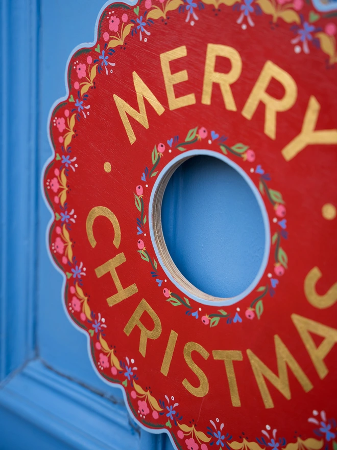 Red Hand painted Christmas Wreath with red lettering and gold leaf lettering on a blue front door