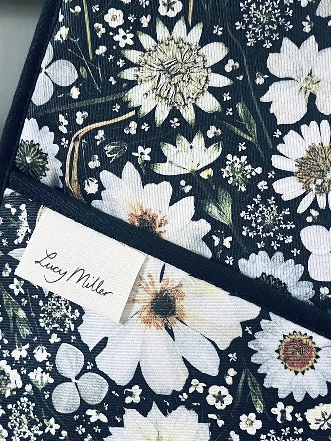 Floral double oven gloves with pressed white flower design on a black background. Complete with hanging loop.