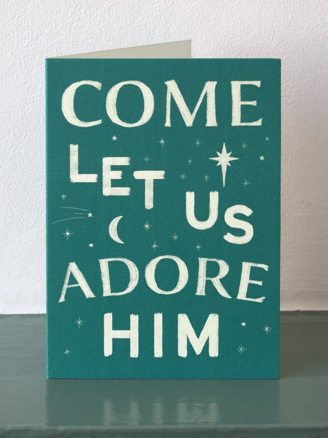 Green Christmas card with the words 'come let us adore him' on the front