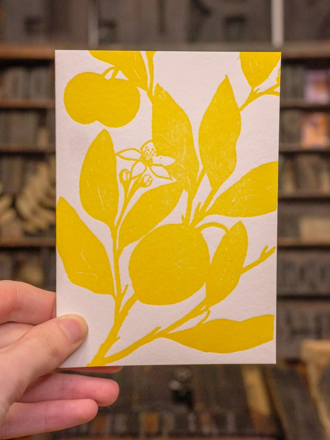 Card held up. Situation shot. Design on front visible: flat shaded monochrome lemon artwork