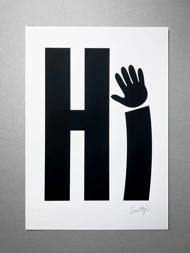 Full view of screenprinted Hi, with a waving hand as the i - sat on a grey background - showing detail of an embossed stamp saying Salty’s
