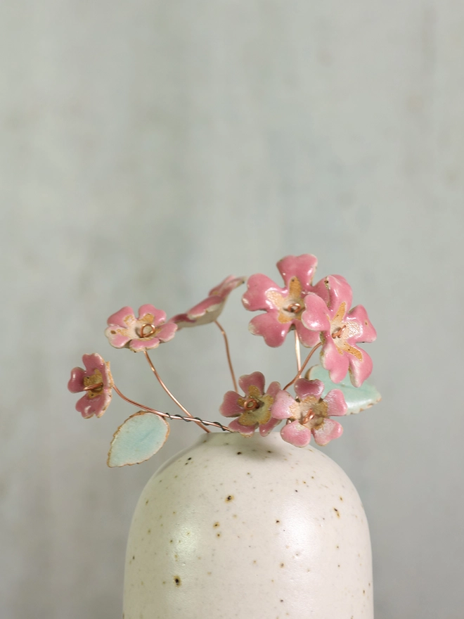 pink cermic primroses burst out of a white stoneware vase against a mottled grey background