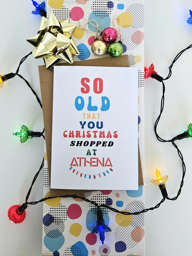 A photograph of the front of a humorous A6 greeting card illustrated using brightly coloured text and the retro shop logo. The text says so old you Christmas shopped at Athena