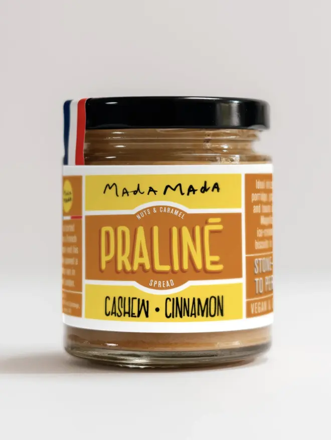 jar of cashew cinnamon praline nut spread with orange and yellow label, and black lid