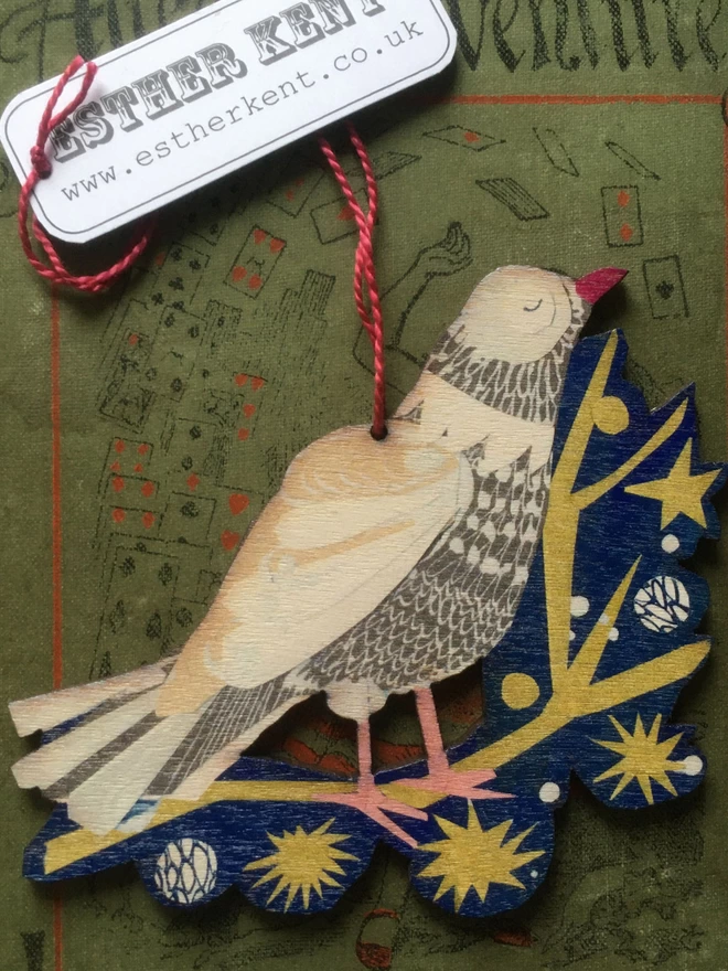 Illustrated peace dove standing on a gold star-spangled twig on a blue backroung. The cut-out decoratiojn rests on a green vintage book