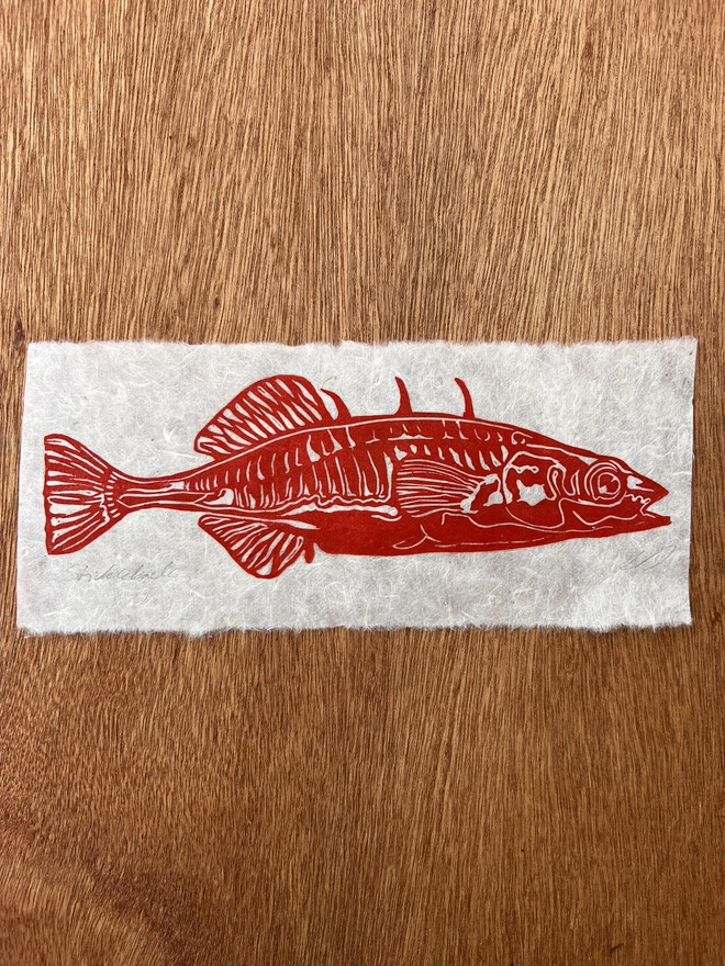 Hand-printed red stickleback fish lino print on natural handmade paper, featuring a bold graphic illustration of a stickleback fish.