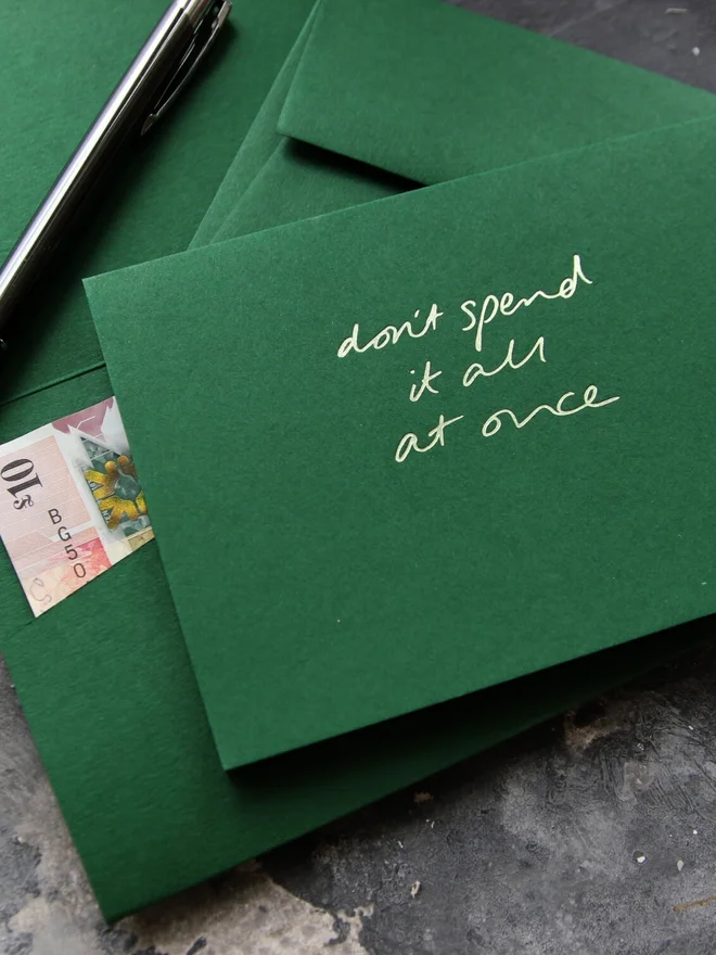 Hand foiled cash card or money wallet in a forest green colour handfoiled in shiny lime green text which says 'don;t spend it all at once'.