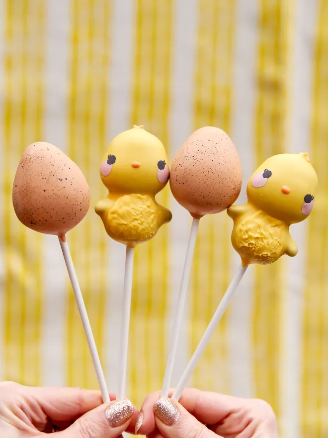Easter Chick&Egg cake pops held up against a white and yellow backdrop 