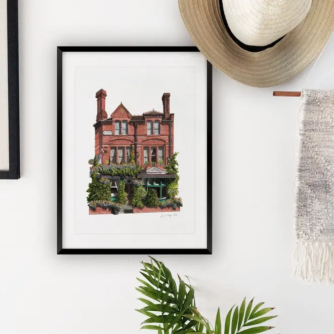 Nunhead Skehans Giclée Print (Unframed), a print of a brick pub in a black frame against a plain backdrop in a living room. 