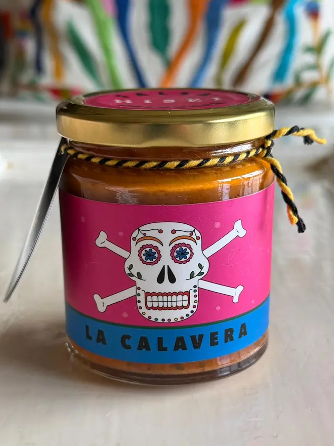 'El Calavera' Salsa Jar (Set Of 1-4 Jars), a jar of salsa sitting on a kitchen counter top. It has the icon of a skull on it. 