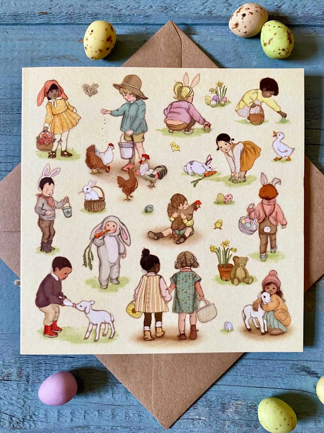 beautifully illustrated easter greeting card featuring vintage style illustrations of children doing Easter things. Easter egg hunt, feeding lambs and chicks shown laid on a kraft envelope surrounded ny mini easter eggs