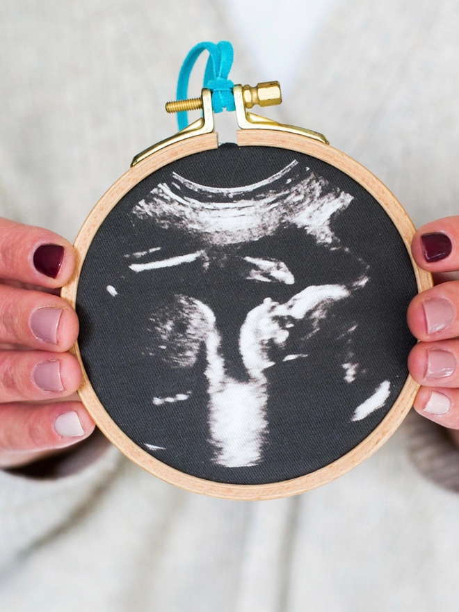 Baby scan photo printed on fabric fixed in an embroidery hoop being held in 2 hands