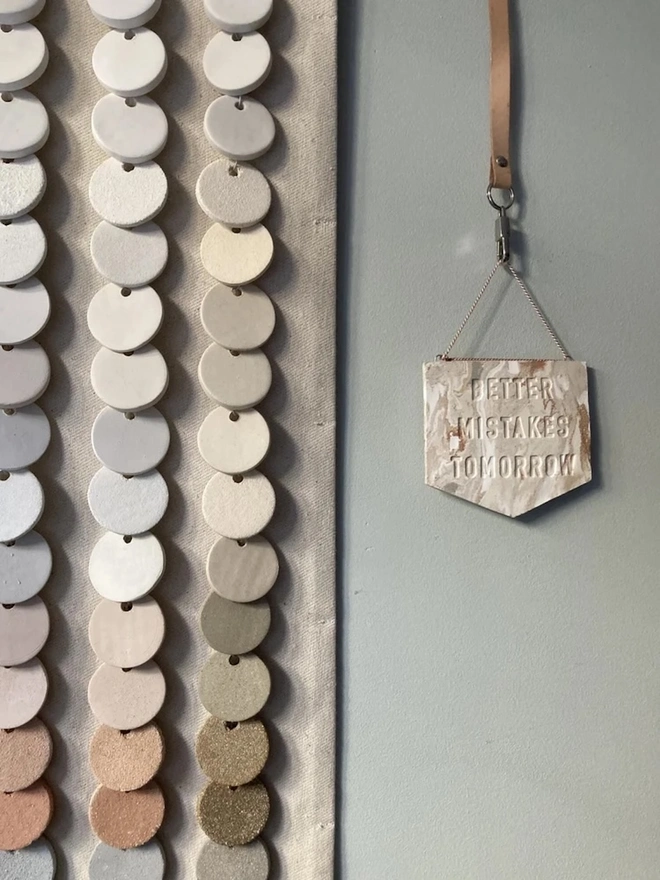 'Better Mistakes Tomorrow' Banner, a clay banner hanging against a plain backdrop.