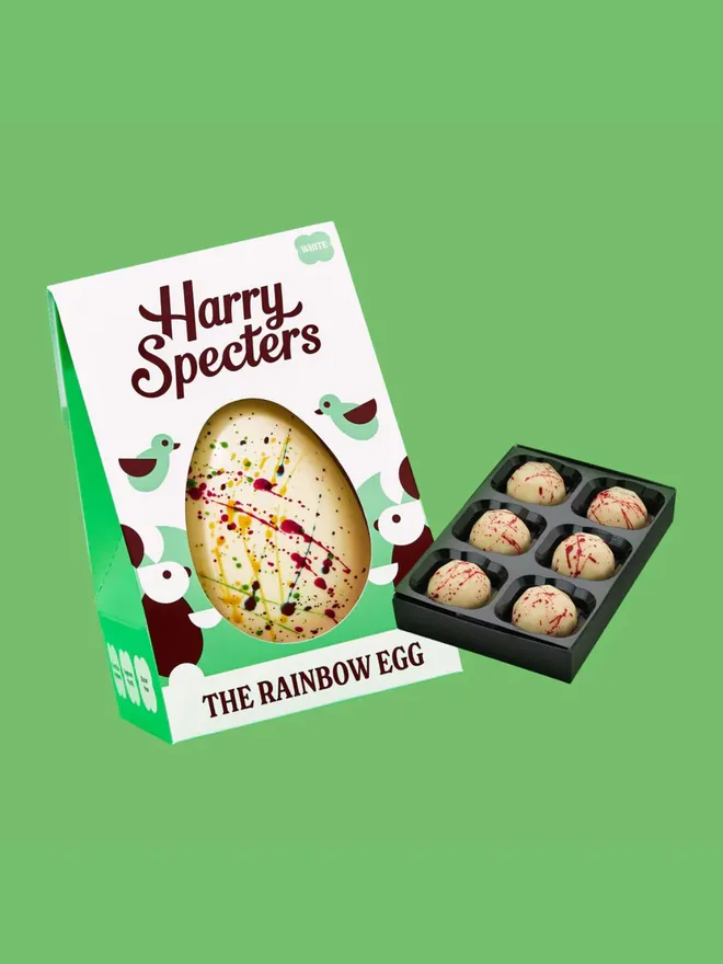 A white chocolate Easter egg decorated with rainbow speckles, next to a small box of luxury white chocolates