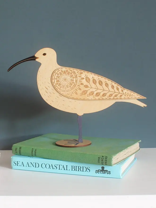 Standing Wooden Curlew, wooden bird decoration standing on a platform on a book. 