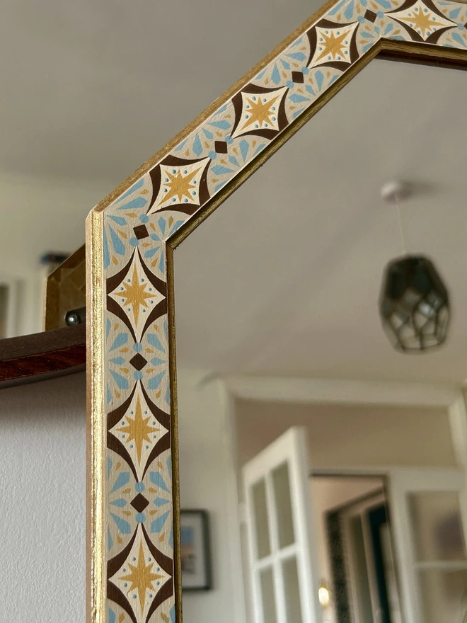 Medium sized octagonal wall mirror with a hand painted decorated frame with gold stars and blue star burst repeating pattern around the frame