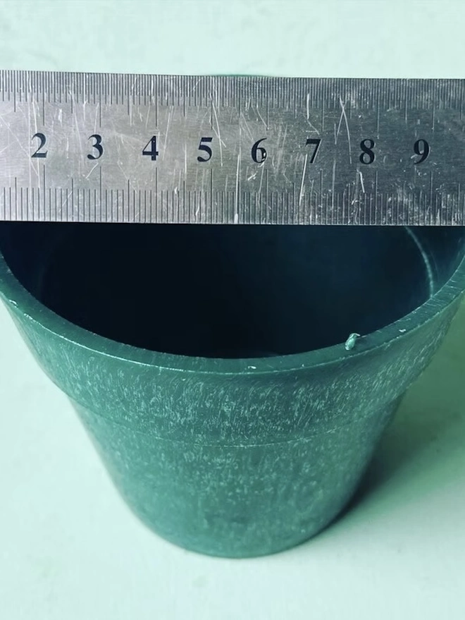 Small Green Ocean Plastic Plant Pot, a green recycled plant pot against a colourful backdrop. 