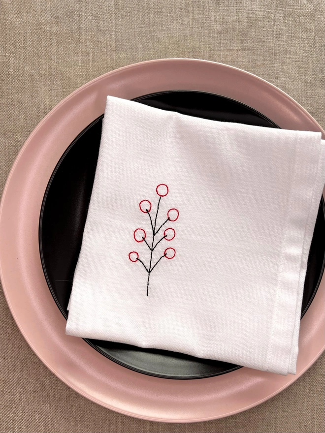 White cotton embroidered Christmas berry napkin, styled on pink and black place setting