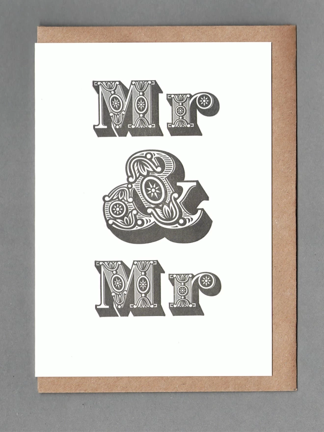 White card with black text reading 'Mr & Mr' with a kraft envelope behind it