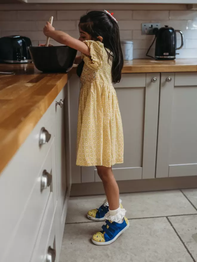 little girl in a yellow dress baking wearing Pip and Henry blue and h=yellow space print sneaker
