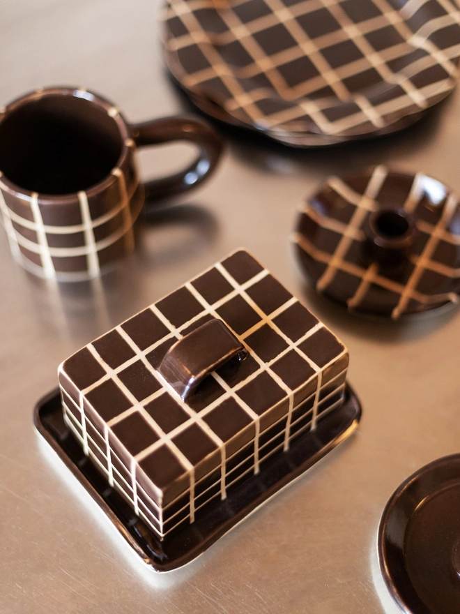 Grid Chunky Mug, a colourful mug with a grid pattern on a white table top surface. It is accompanied by other patterned dishes. 