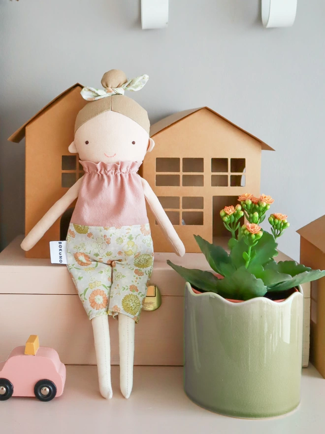 Textile stuffed girl doll with fair skin and pink floral clothes.