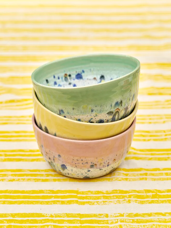 Shoreline Ramen Bowl, a collection of colourful ramen bowls stacked together-green, yellow and pink, placed on a yellow and white striped tablecloth 