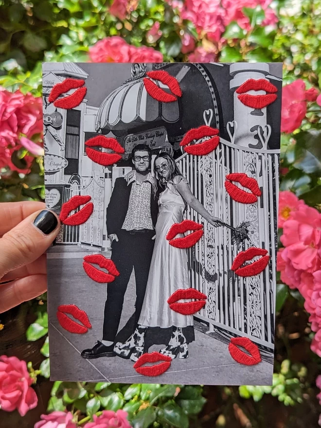 Couples photo, with red embroidered lips, held against pink flowers