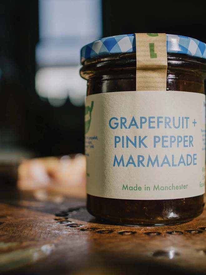 Jar Of Grapefruit & Pink Peppercorn Marmalade, jar of marmalade on a decorated plate on a table. 