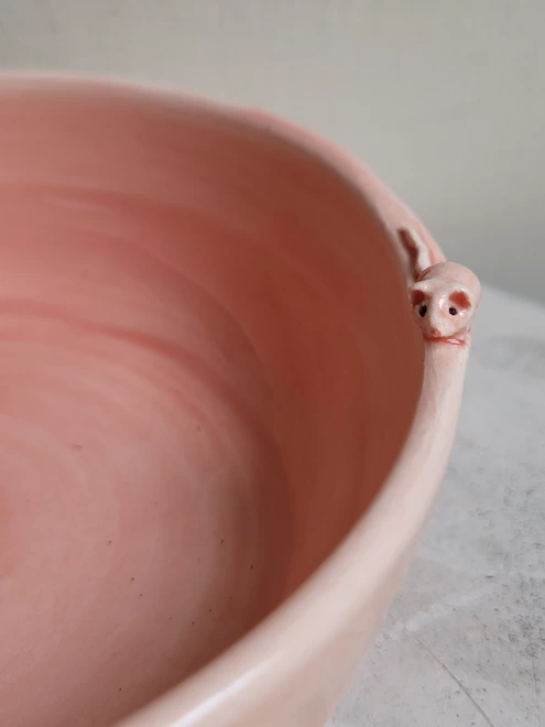 close up of a tiny ceramic mouse attached to the edge of a pink ceramic cat bowl