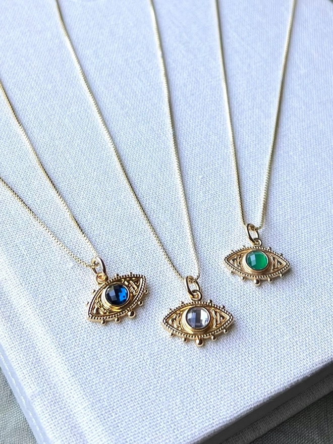 gold evil eye charm necklace on gold box chain with a blue, green and grey quartz stone