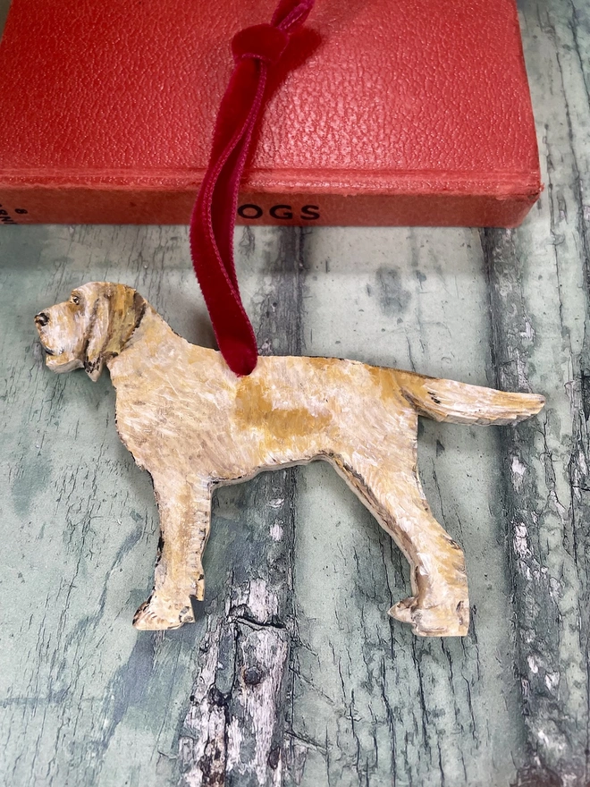 Italian Spinone Dog Christmas decoration with a full tail hung with red velvet ribbon and placed on a book about dogs