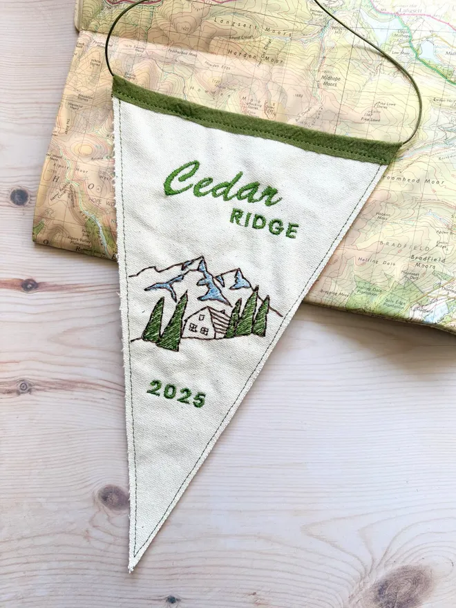 A mini embroidered cabin location pennant flag on a vintage map