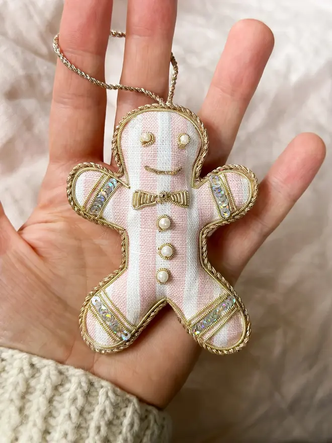 Embroidered Linen Gingerbread Man Decoration. pink and white striped embroidered gingerbread man decoration held in palm