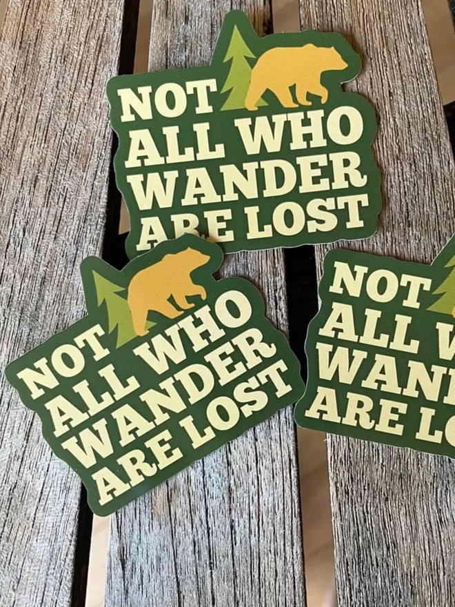 Three Not All Who Are Wander Are Lost Vinyl Stickers on a wooden table.