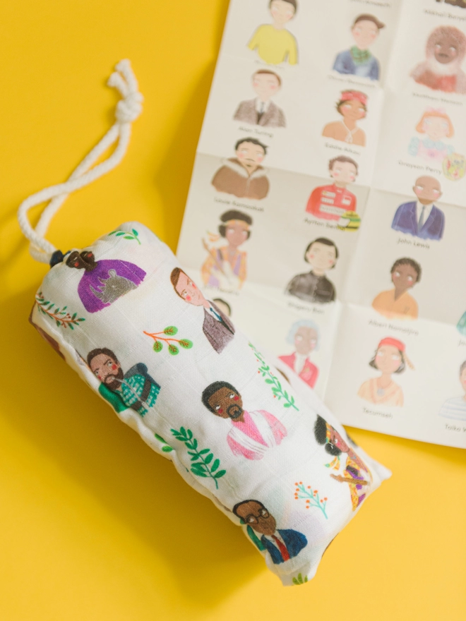 swaddle blanket packaged in drawstring bag, printed with little portraits of inspiring people. Alongside a guide to each portrait featured on the blanket
