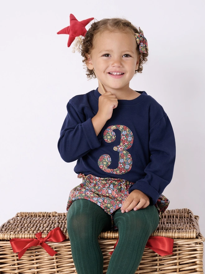 a 3 year old girl wearing a navy birthday t-shirt with a number 3 cut from liberty floral print on the front