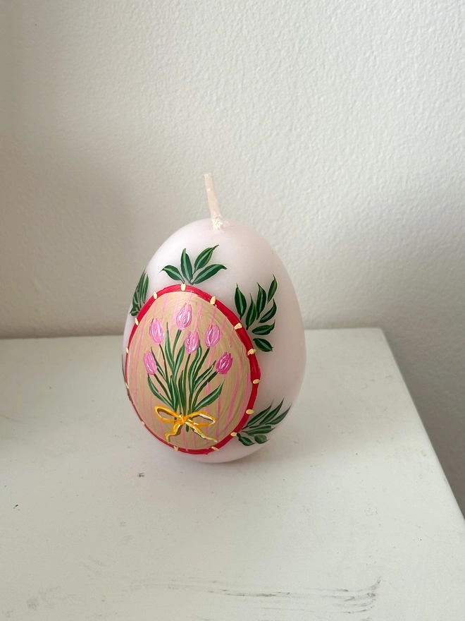 Hand Painted Easter Egg Candle Pink Tulips, an Easter egg candle sitting on a plain surface. It's Easter and floral design wraps around it. 