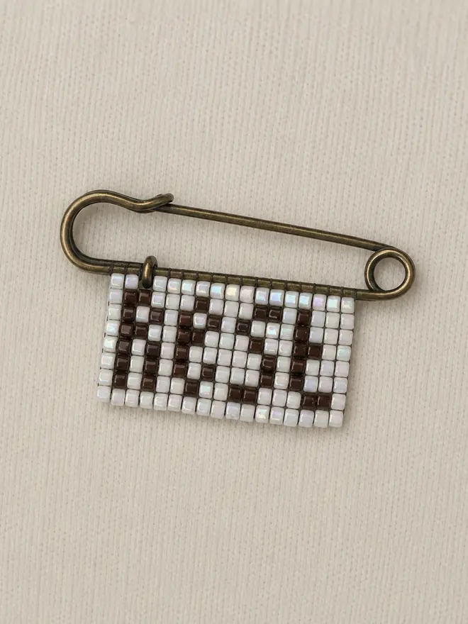 beaded rest pin. a beaded pin badge with the word rest in brown lettering on a pearl background.