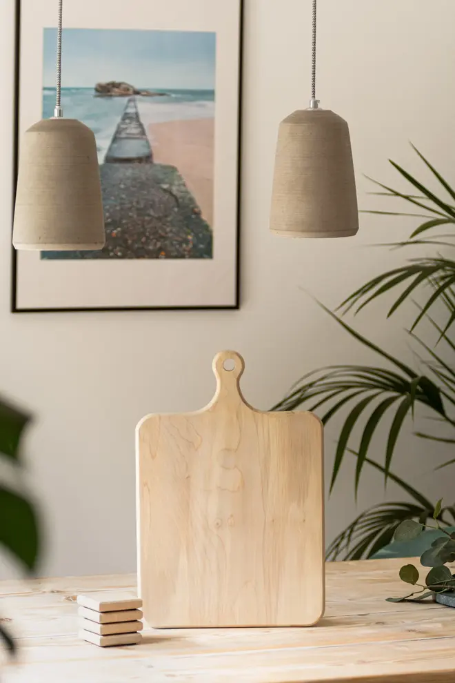 Sycamore Square Serving Board, a wooden serving board sitting in a kitchen. It is accompanied by a picture in the background. 