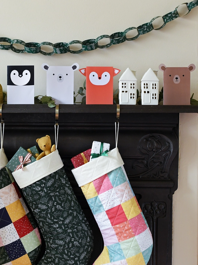Several animal shaped greetings cards stand on a black mantlepiece where two patchwork stockings are hanging from.