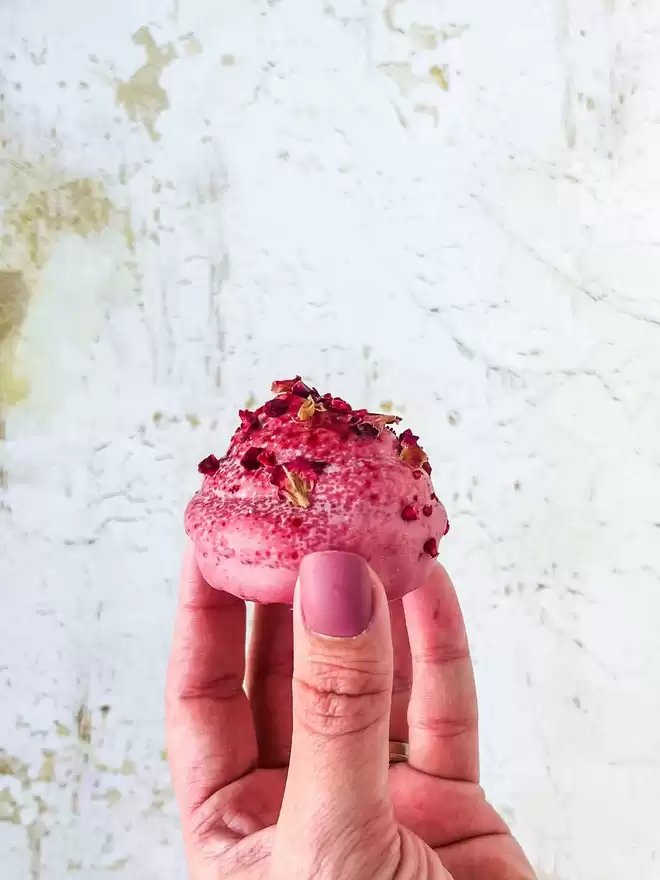 a person holding a pink chocolate covered marshmallow and macaron treat shaped like little kisses in their hand