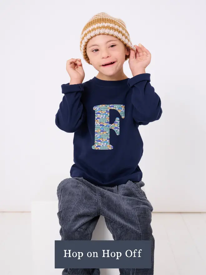 a 4 year old boy wearing a personalised kids personalised navy t-shirt with an initial cut from hop on cars and busses liberty print on the front