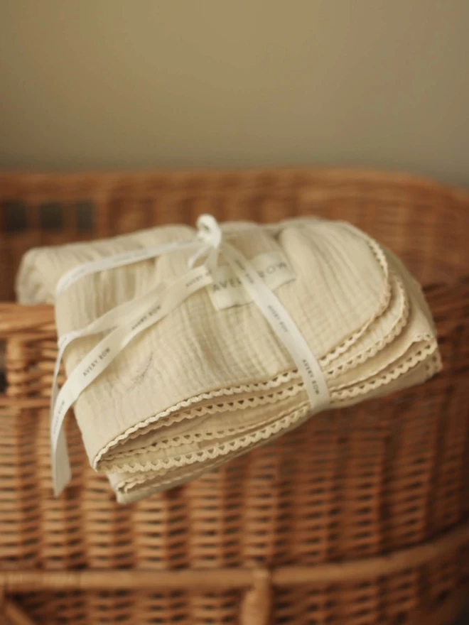 An embroidered muslin blanket in grasslands, milky white colour placed on top a changing basket