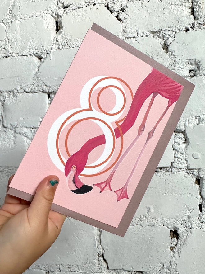 a pink card with a big white number 8 and an illustrated flamingo with a purple envelope